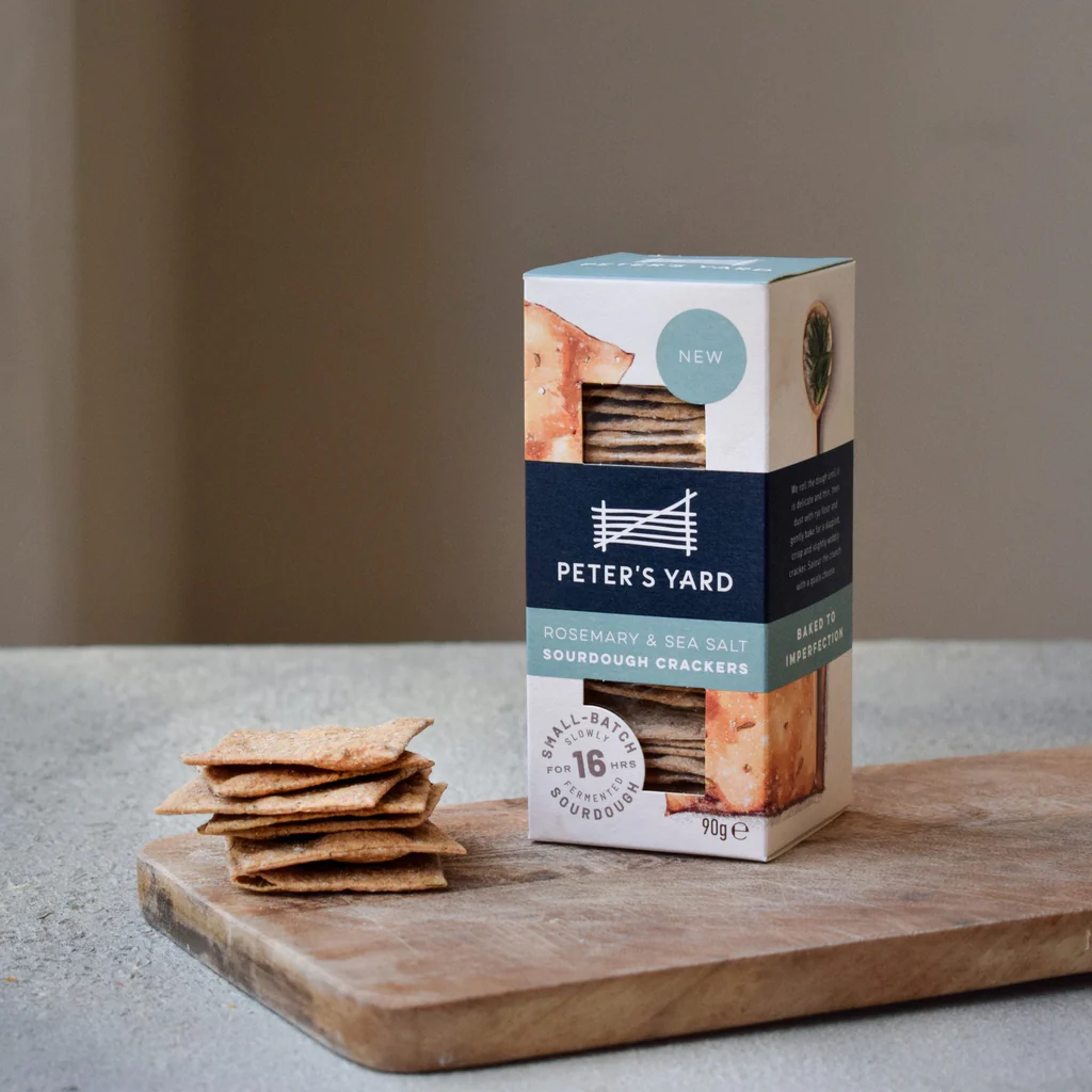 Box of crackers on wooden chopping board with loose crackers